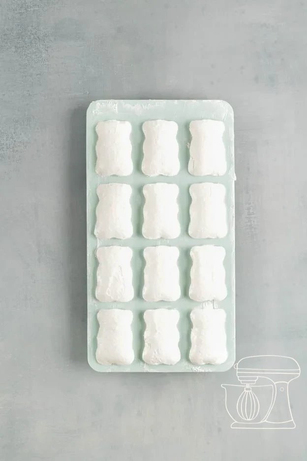 Baked white meringue bears cooling in the silicone mold on the perforated tray