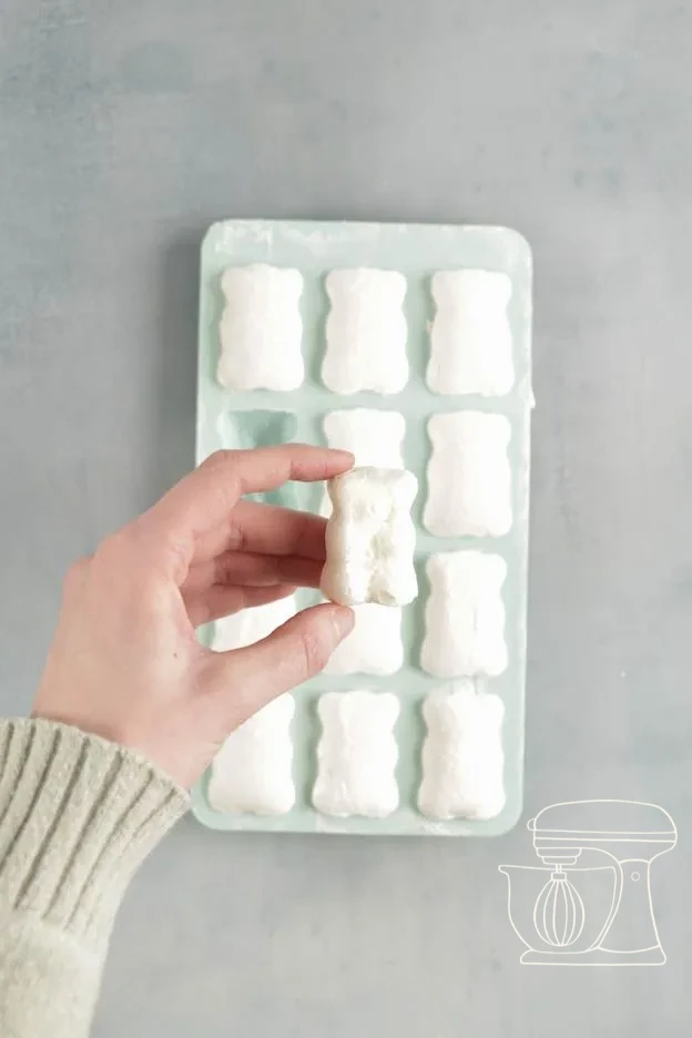 Baked white meringue bears cooling in the silicone mold on the perforated tray