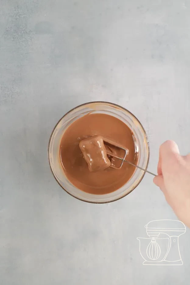 Meringue bear being dipped into tempered milk chocolate with the dipping fork