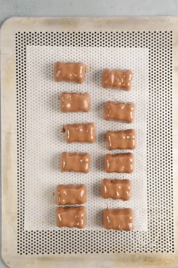 Meringue bear being dipped into tempered milk chocolate with the dipping fork